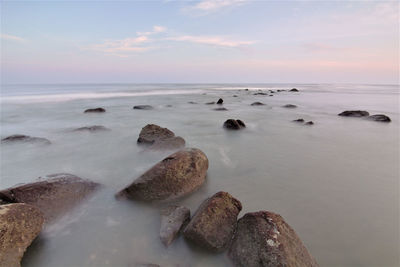 Rocks at sea shore against sky during sunset