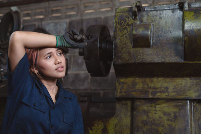 Female factory worker wiping sweat from her head with her arm looking away from camera