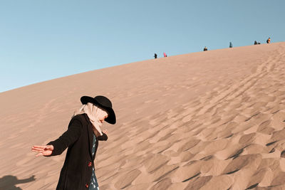 Man and woman on sand dune in desert against clear sky