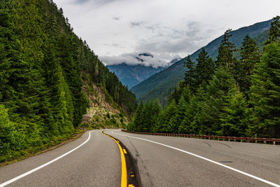 Road amidst trees and mountains against sky