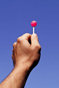 Cropped image of hand holding lollipop candy against clear sky
