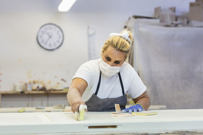 Woman sanding wood while standing by workbench at workshop