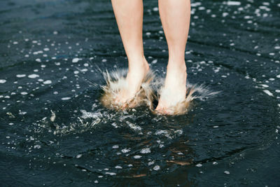 Low section of woman splashing water on lake 