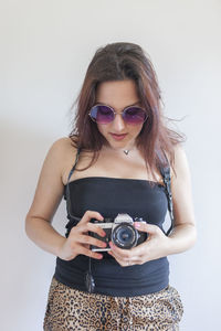 Young woman wearing sunglasses standing against wall