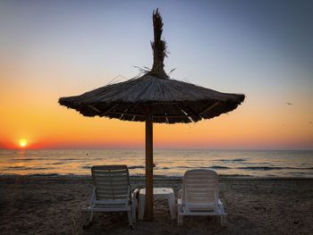 Thatched roof umbrella and two sunbeds on the beach at sunrise
