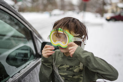 A small child plays outside in snow with a large snorkel mask on face