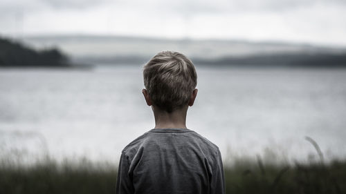 Rear view of boy standing on field against sea