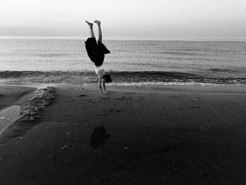 Girl doing handstand at beach against sky