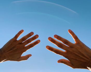 Low angle view of hands gesturing against blue sky