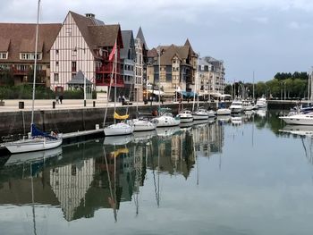 Sailboats moored on river in trouville-sur-mer, france, by buildings against sky
