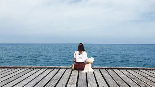 Rear view of woman sitting on sea against sky