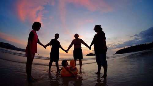 People ay beach against sky during sunset