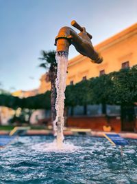 Digital composite image of faucet with running water against building