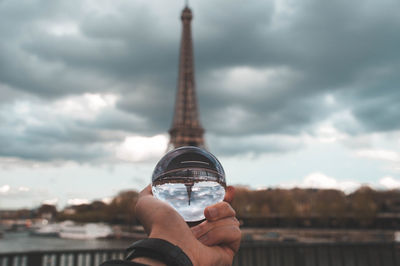 Man holding crystal ball with reflection of eiffel tower against cloudy sky