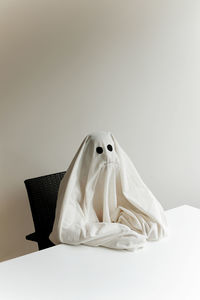 Man in ghost costume sitting by table against wall at home during halloween