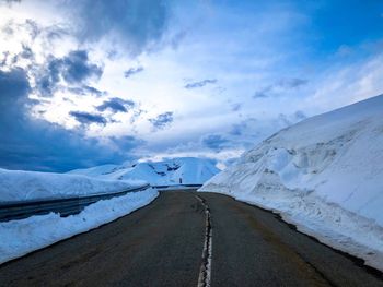 Road amidst snowcapped mountains against sky during winter