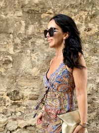 Young woman wearing sunglasses standing against wall