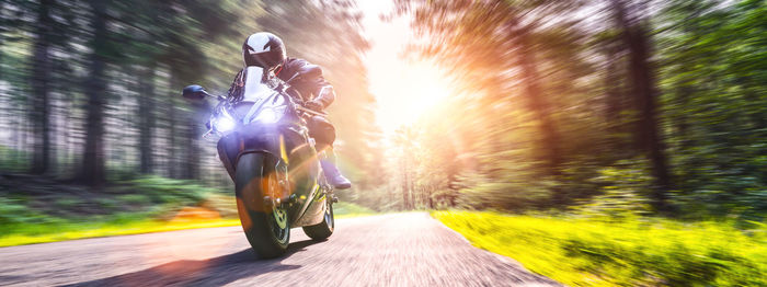 Blurred motion of person riding motorcycle on road amidst trees