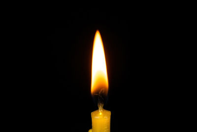 Close-up of burning candle against black background