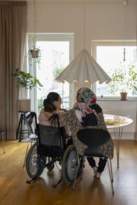 Woman sitting on wheelchair by mother at dining table