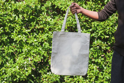 Midsection of man holding bag against plants