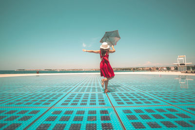 Woman standing by swimming pool against blue sky