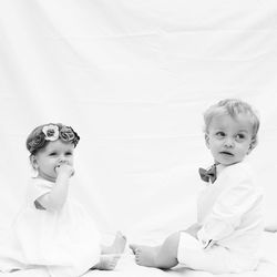 Side view of siblings looking away while sitting against curtain