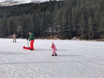 Family enjoying at snow covered field against trees