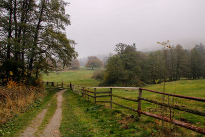 Dirt road amidst field against sky