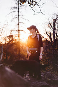 Woman standing by dog in forest during sunset
