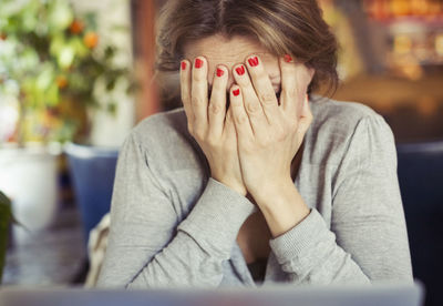 Sad young woman sitting with head in hands at home