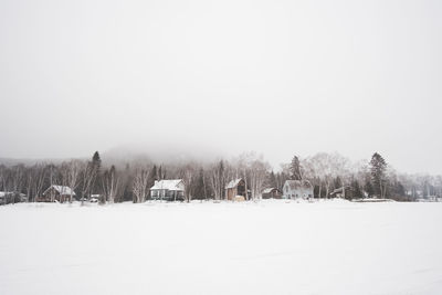 Trees on snow covered field against sky