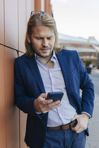 Businessman using mobile phone at wall