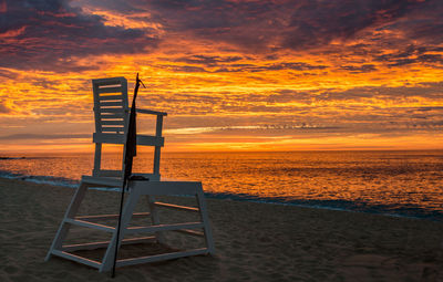 Lifeguard chair at beach against sky during sunset