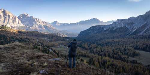 Photographer with camera on tripod taking picture of beautiful valley during sunrise in dolomites