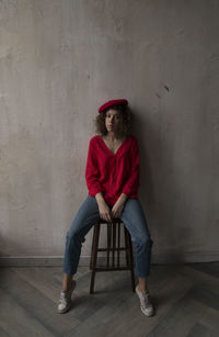 Full length portrait of young woman sitting against wall