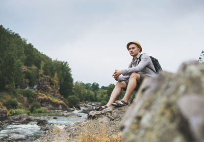 Full length of man sitting on rock against sky