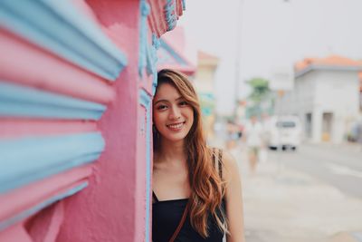 Portrait of young woman standing by wall in city