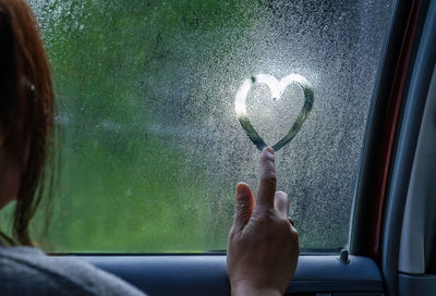 Midsection of woman holding heart shape seen through car window