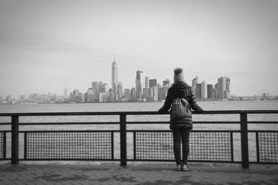 Rear view of woman standing by railing against river