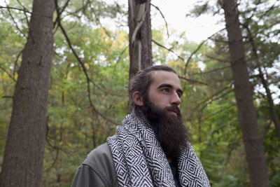 Portrait of young man standing by tree trunk in forest