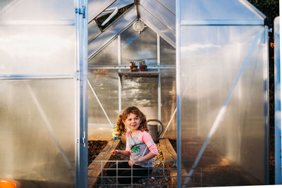 Young girl sitting alone in backyard greenhouse during spring time