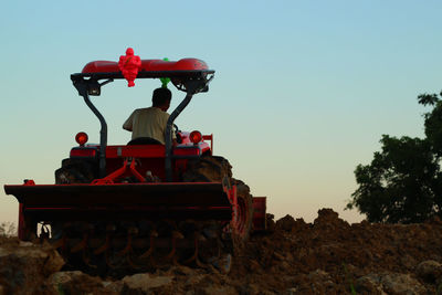 Rear view of man in tractor ploughing field against sky