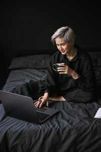 Woman working at home with laptop, drinking coffe, black colors interior