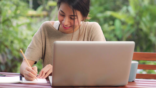Young woman using mobile phone while sitting on table