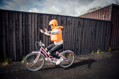 Smiling girl riding bicycle with arms outstretched on road