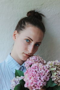 Close-up portrait of woman with flowers against white wall