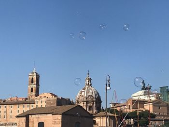 Low angle view of bubbles and buildings against clear blue sky