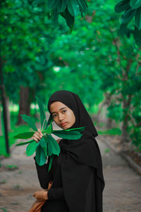 Portrait of young woman standing against plants