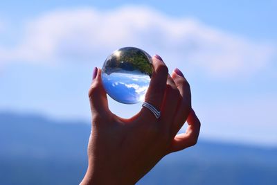 Midsection of person holding crystal ball against sky